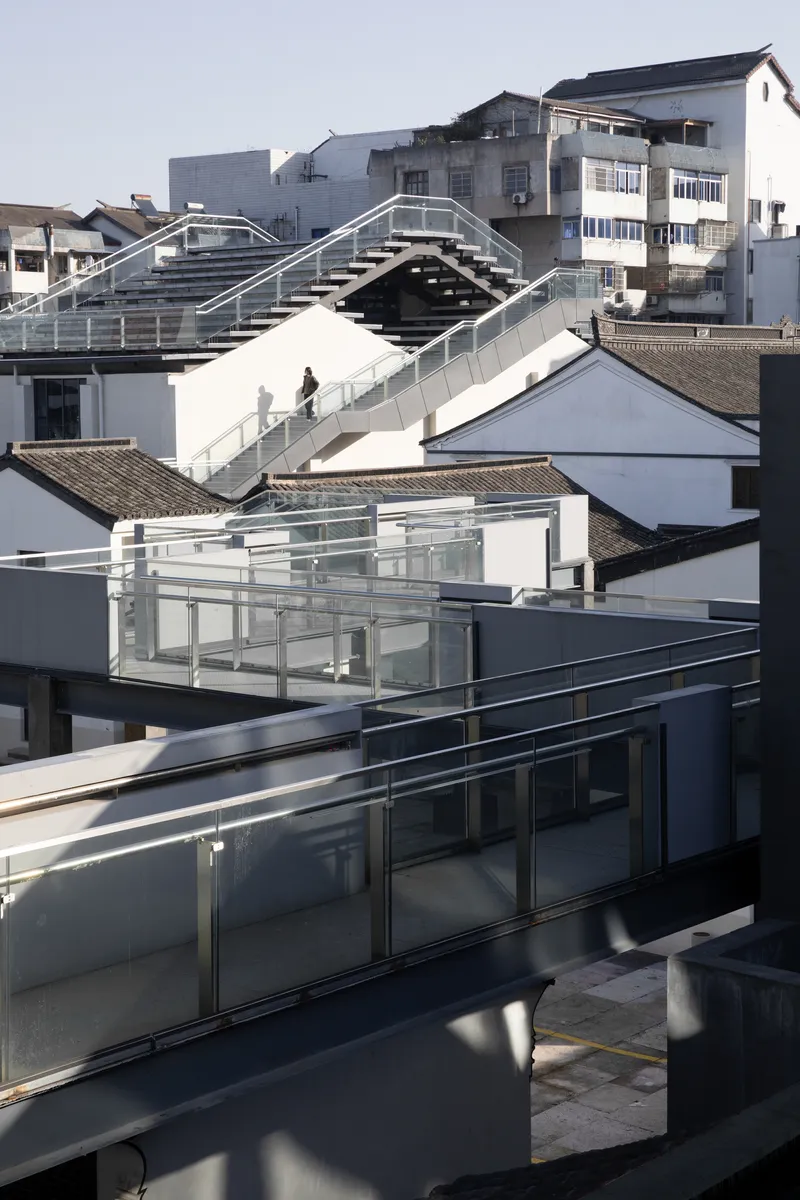 Arched pedestrian bridge spanning between white buildings above traditional pitched roofs in daylight