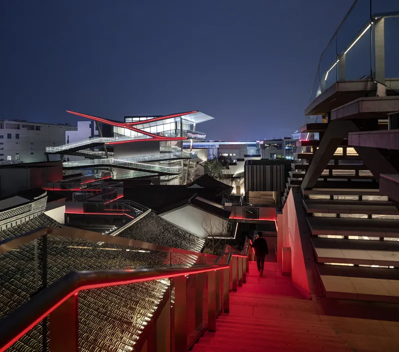 Red-lit exterior staircase descending between courtyards and white cantilevered roof at dusk