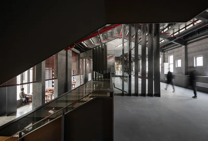 Mezzanine corridor with red steel trusses and glass balustrade overlooking exhibition spaces below