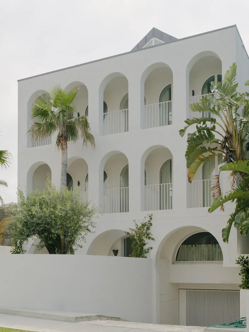 White stucco facade with arched openings and white balustrades, framed by palms and tropical foliage