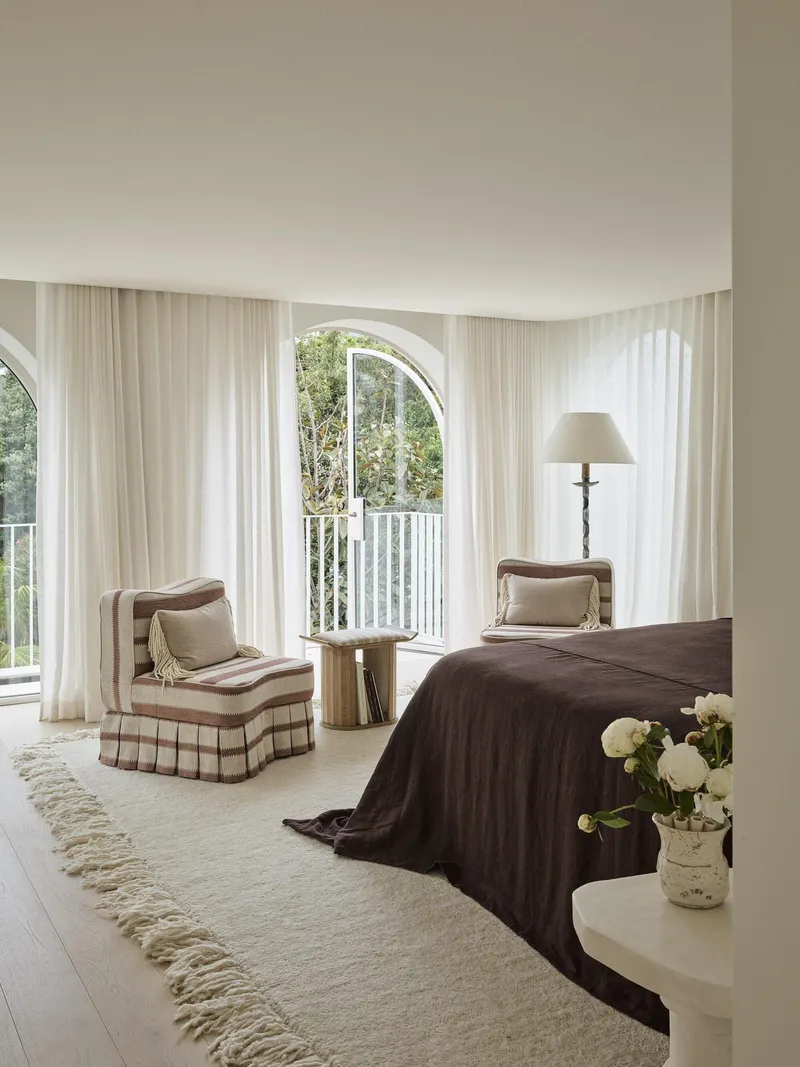 Bedroom with sheer curtains framing an arched door opening to a balcony with garden views