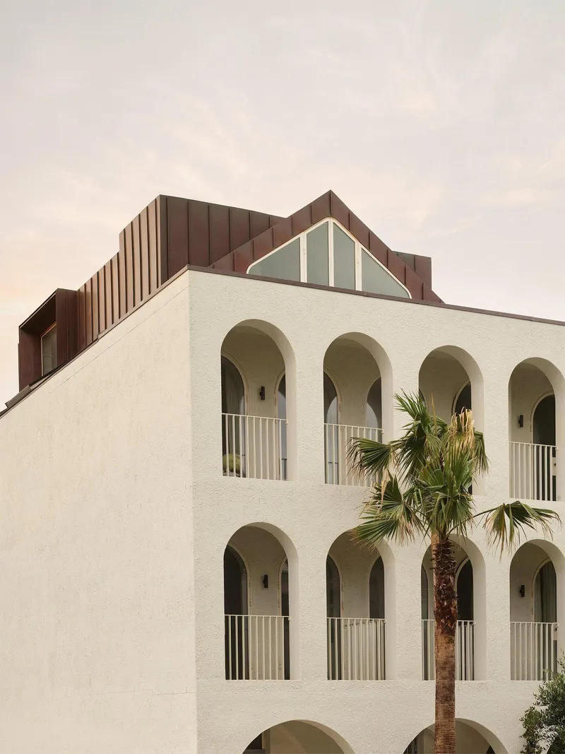 White stucco facade with arched balconies and a palm tree framed against a soft evening sky
