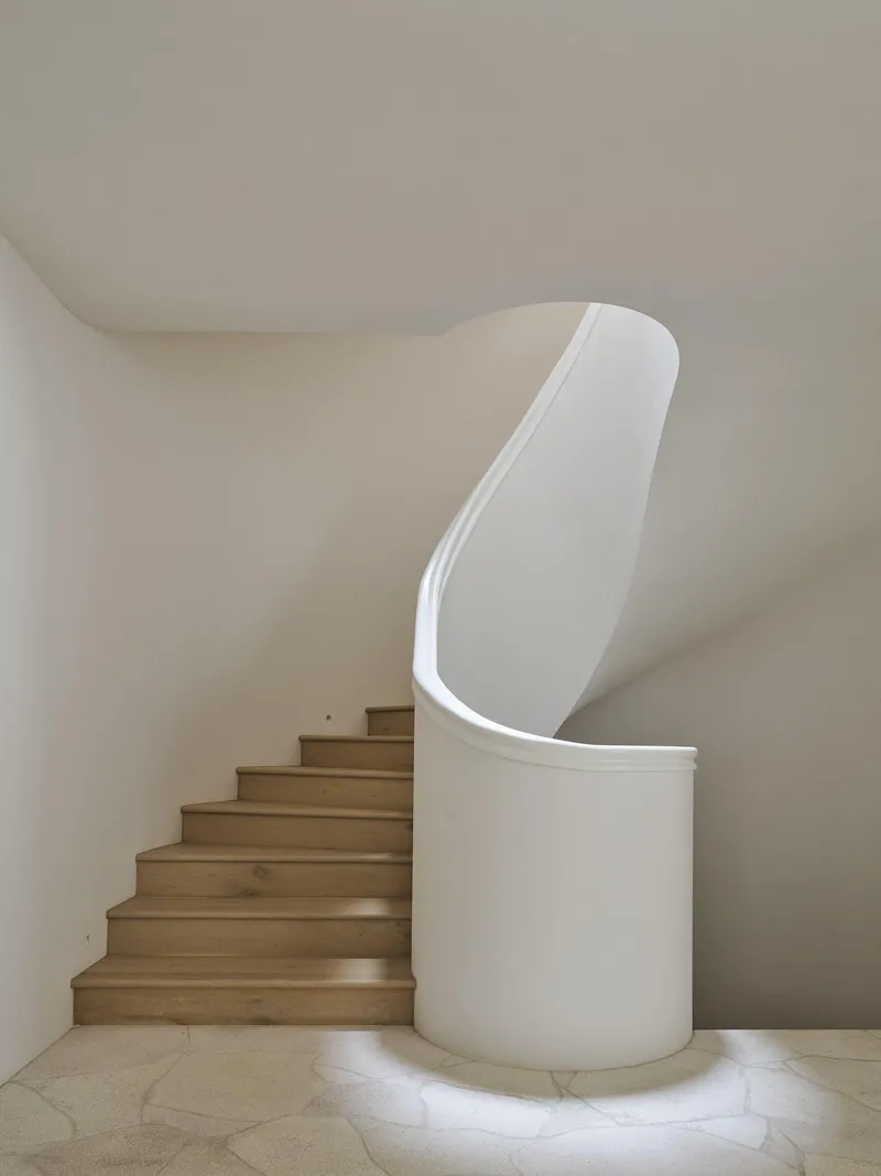 Curved timber staircase with integrated white plaster balustrade illuminated by concealed floor lighting