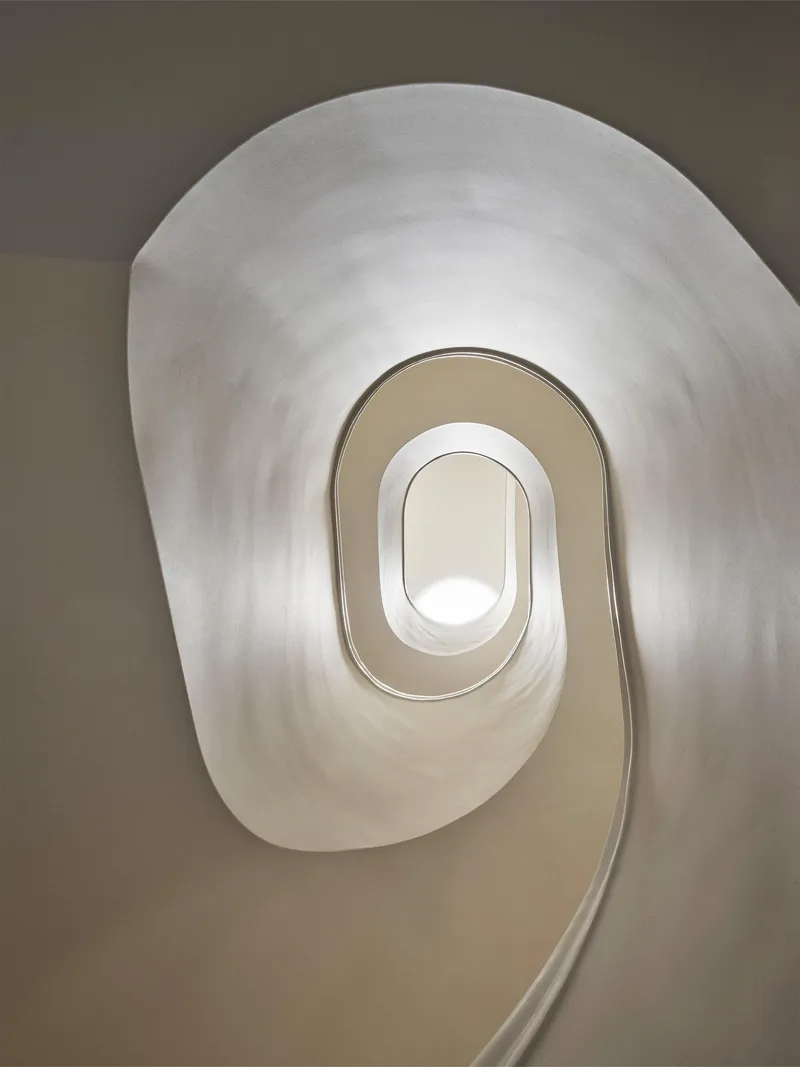 Looking up through an oval-shaped spiral stairwell with smooth plaster walls in natural light