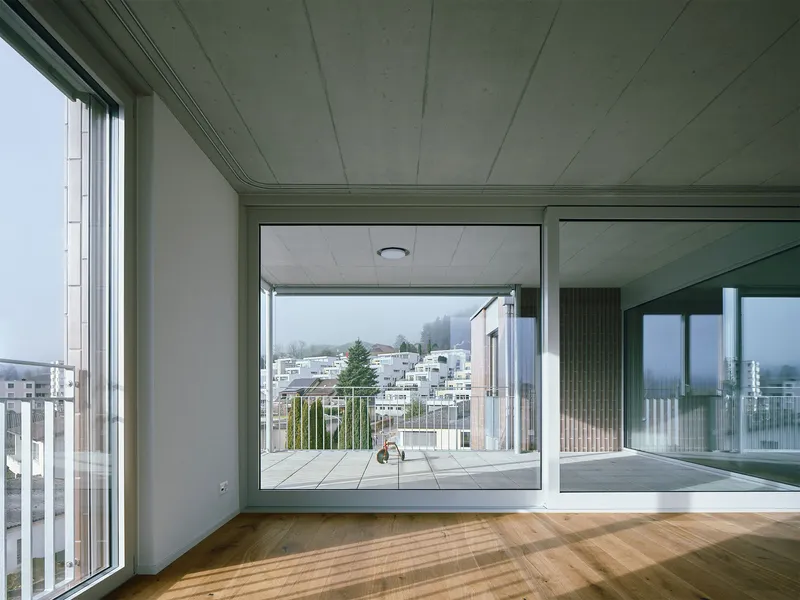 Living room with floor-to-ceiling glazing framing a tiled balcony and distant hills in mist