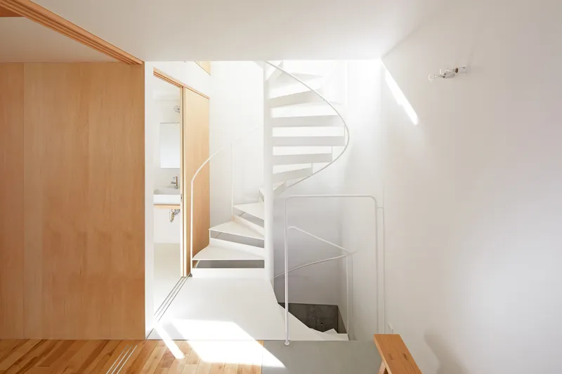 White spiral staircase ascending between timber-framed doorways in a sunlit interior
