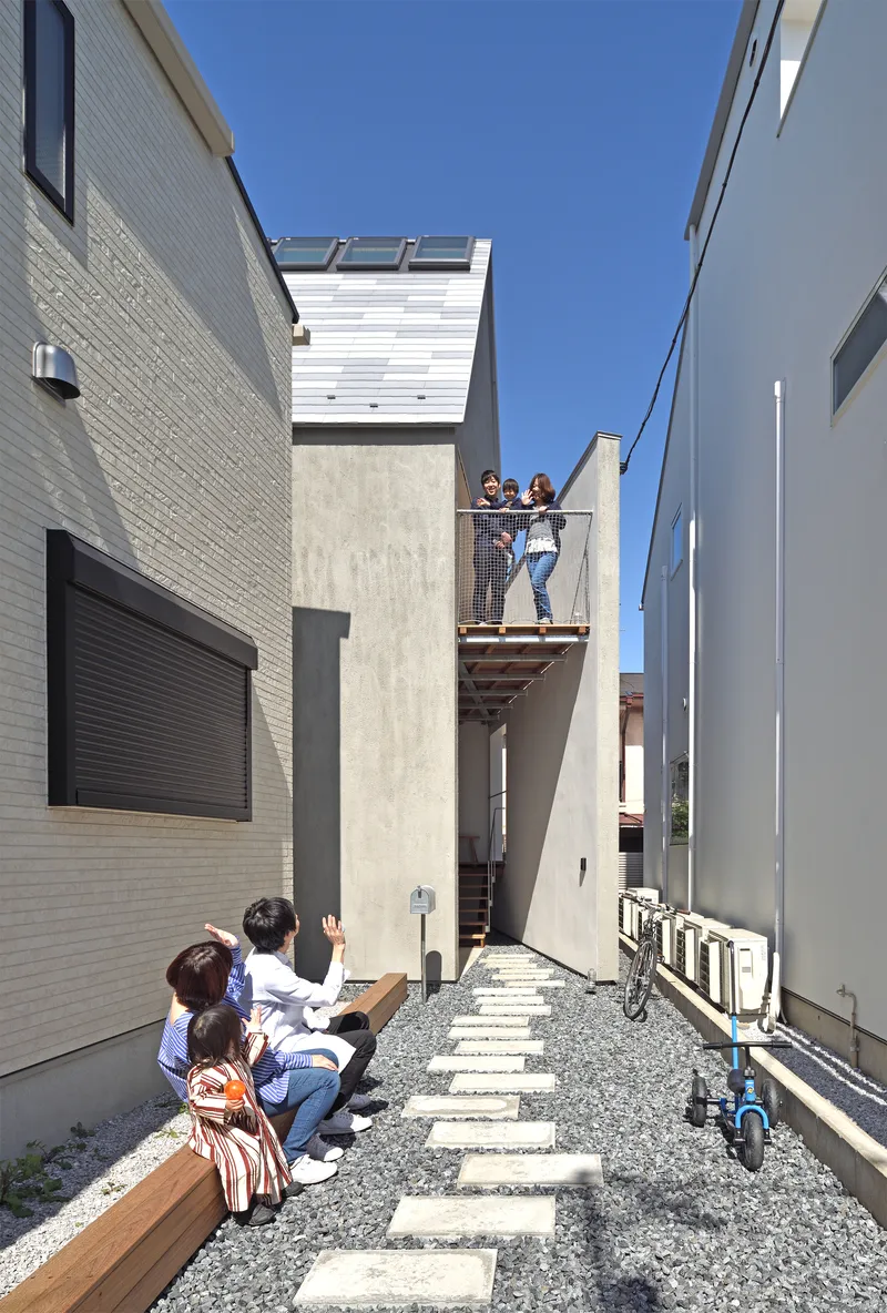 Narrow side courtyard with stepping stone path where residents gather below a cantilevered balcony