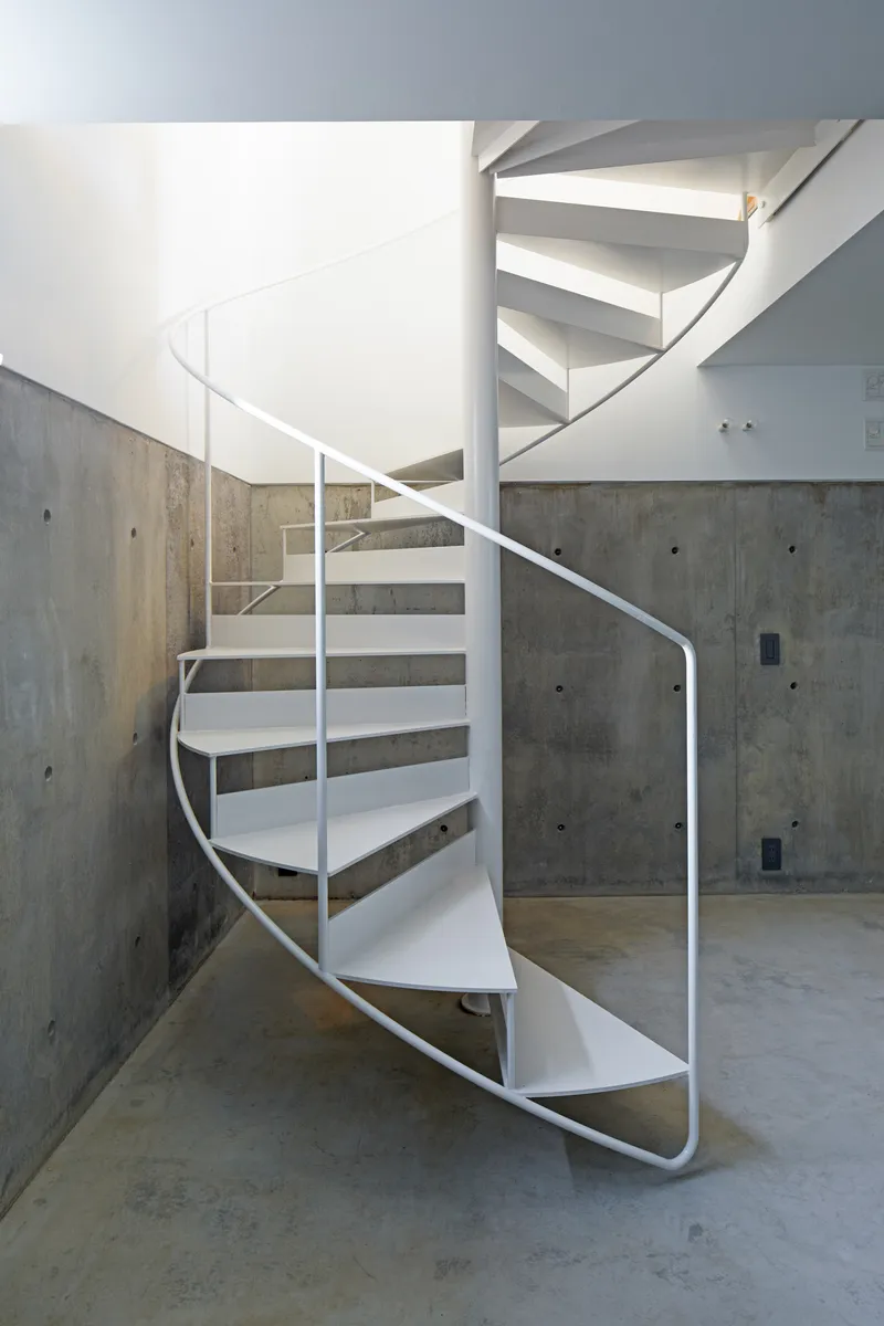 White metal spiral staircase against board-formed concrete walls with visible tie holes