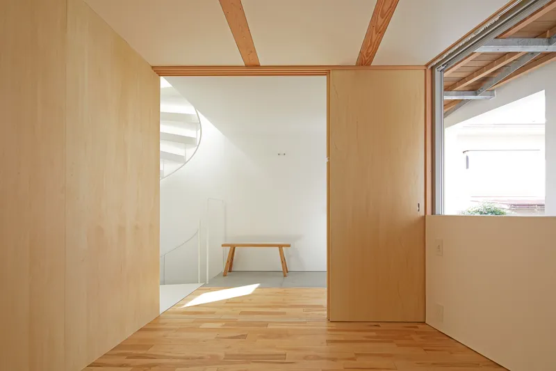 View through plywood-lined rooms with exposed timber beams and a wooden bench in sunlight