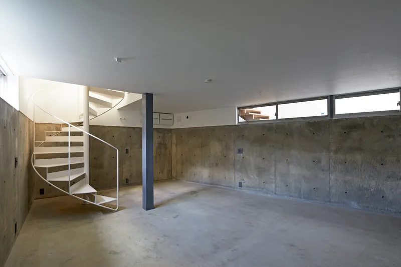 Lower level space with board-formed concrete walls, spiral stair, and steel column under clerestory windows