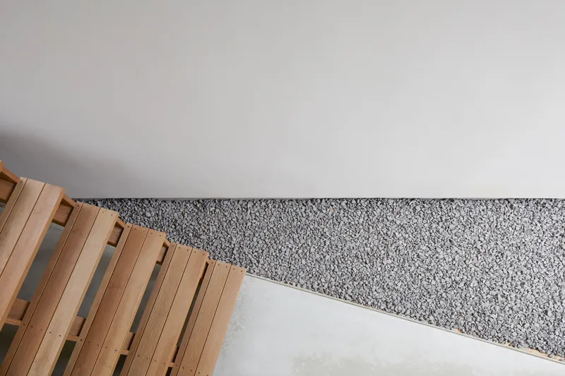 Overhead view of timber deck edge meeting a gravel courtyard beside white rendered wall