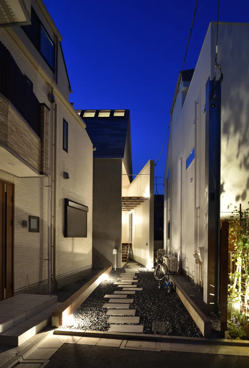 Narrow alley with stepping stone path through black gravel leading to illuminated white houses at twilight