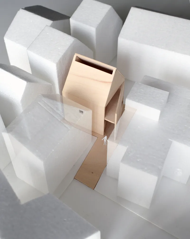Physical model of a slender timber house form surrounded by white foam block massing