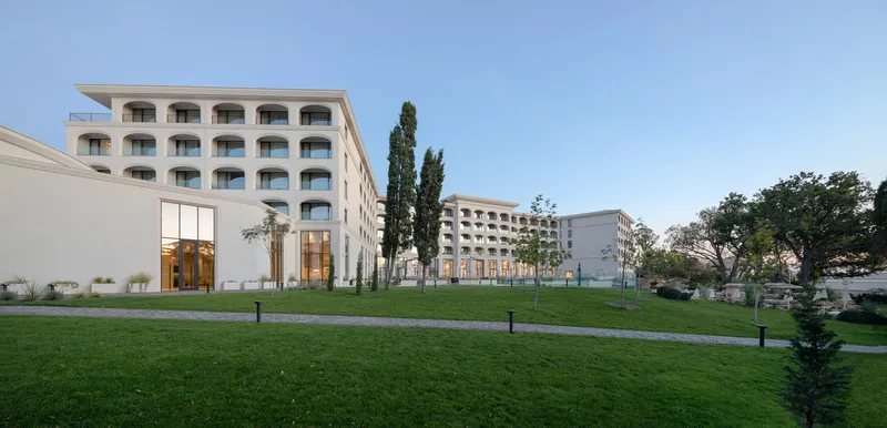 View across the lawn toward the arched facade and low glazed entry volume under blue sky