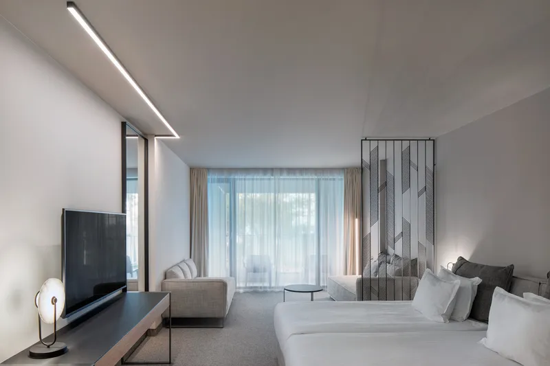Guest room with twin beds and sheer curtains filtering daylight through floor-to-ceiling windows