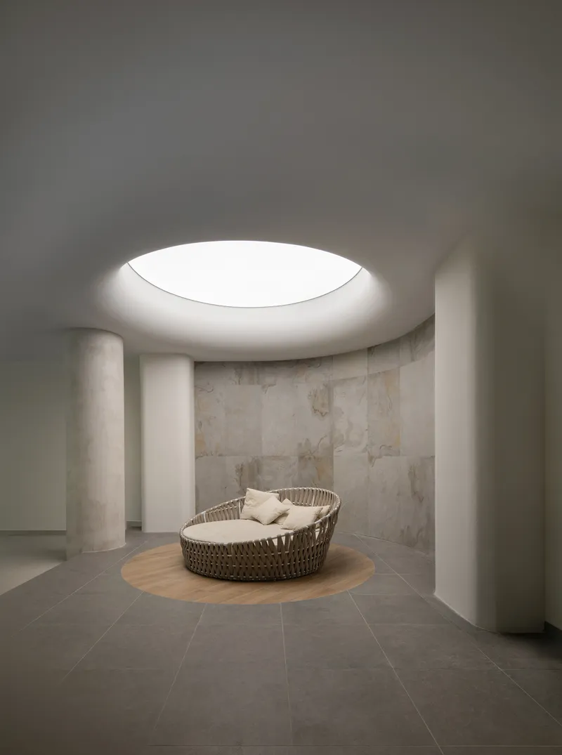 Circular spa room with round daybed beneath a glowing oculus skylight and limestone walls