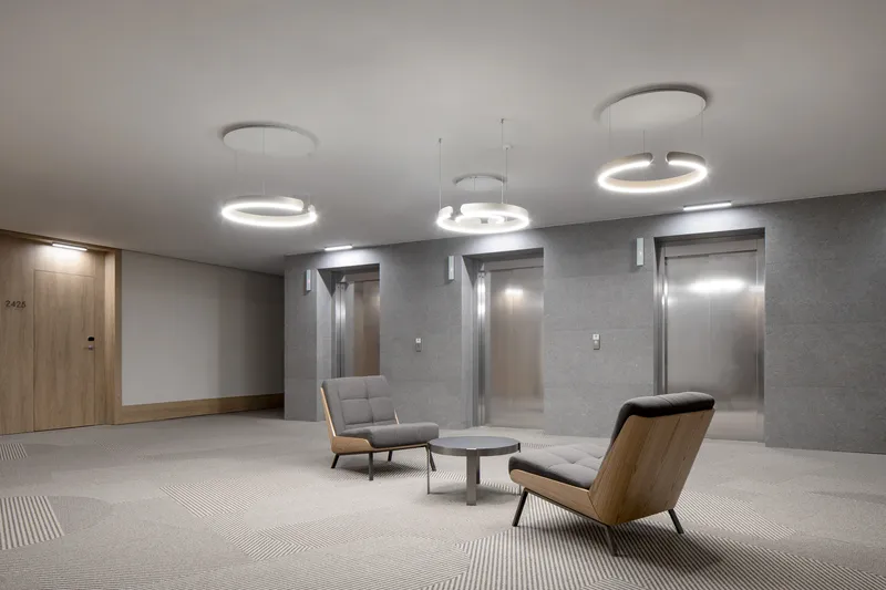 Elevator lobby with circular pendant lights suspended above upholstered lounge chairs and grey textured walls