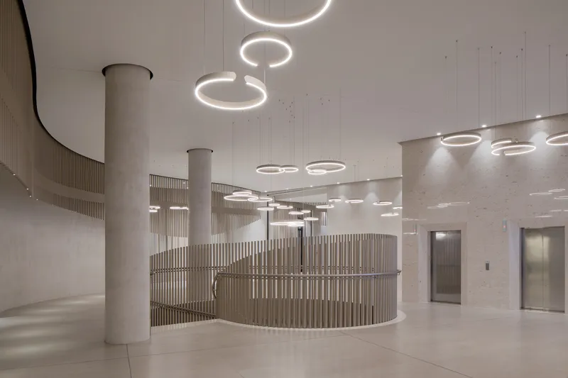 Reception area with curved slatted timber desk enclosure beneath cascading ring chandeliers and concrete columns