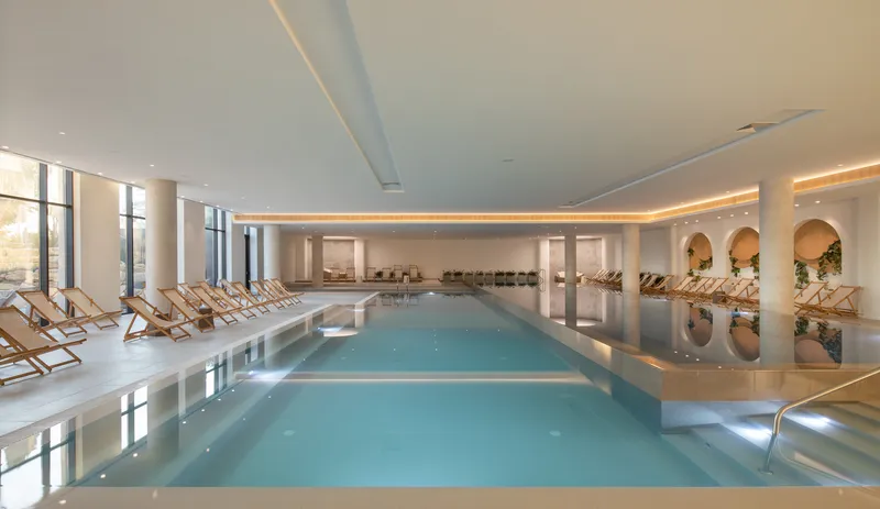 Indoor pool with arched niches and rows of loungers reflected in the still water