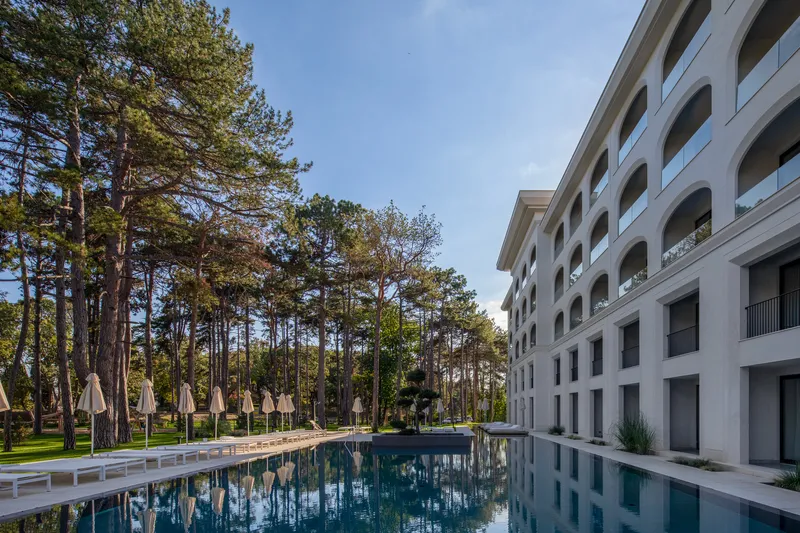 Reflecting pool alongside the arched balcony facade with pine trees beyond