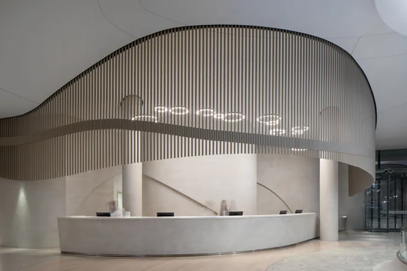 Reception desk with curved stone face under a flowing slatted screen and pendant lights