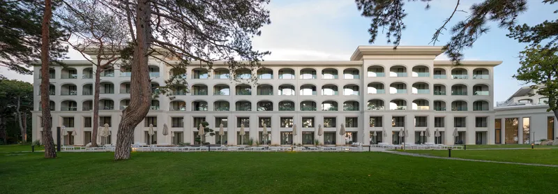 Long facade of arched balconies across the lawn with pines in the foreground