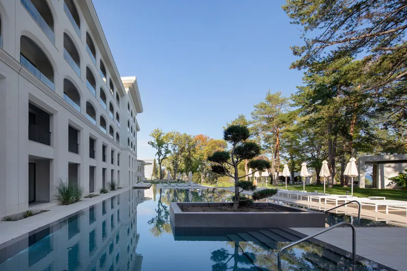 Reflecting pool running alongside the white facade with arched openings and planted courtyard