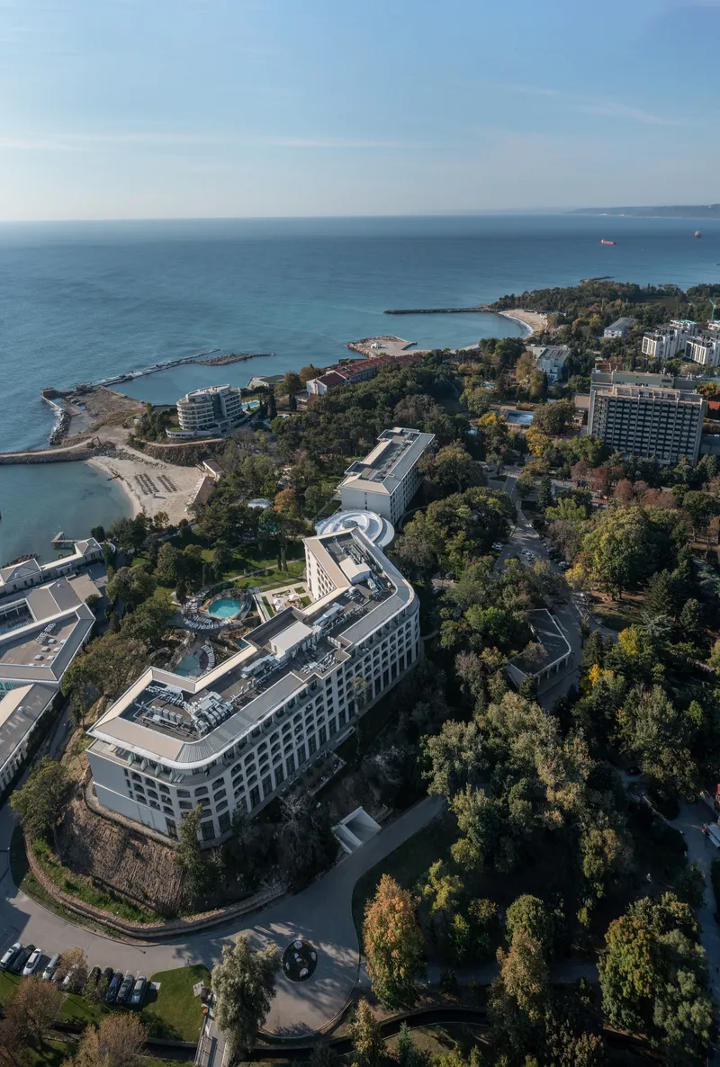 Aerial view of the curved white building with rooftop pool nestled in forested coastline