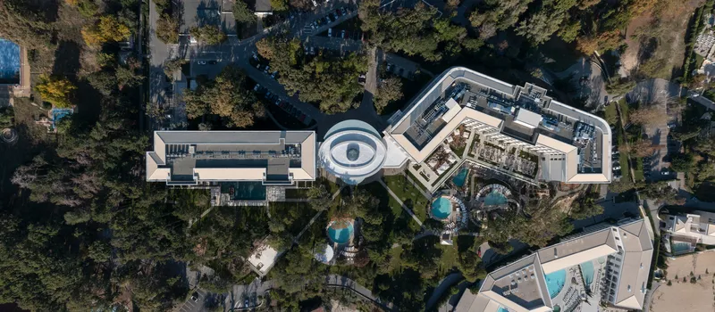 Drone view of the complex showing curved rooftops, circular courtyard and surrounding forest