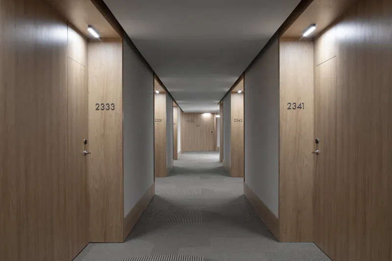 Hotel corridor with numbered wood doors and grey walls under recessed linear lighting