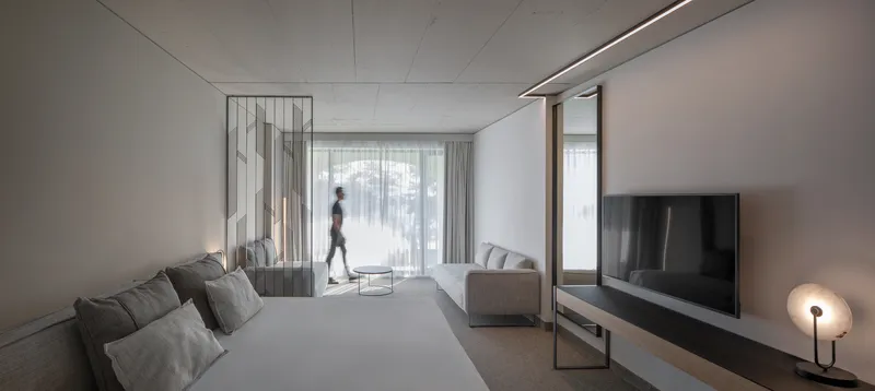Hotel room interior with grey textiles and perforated metal partition separating bed from seating area