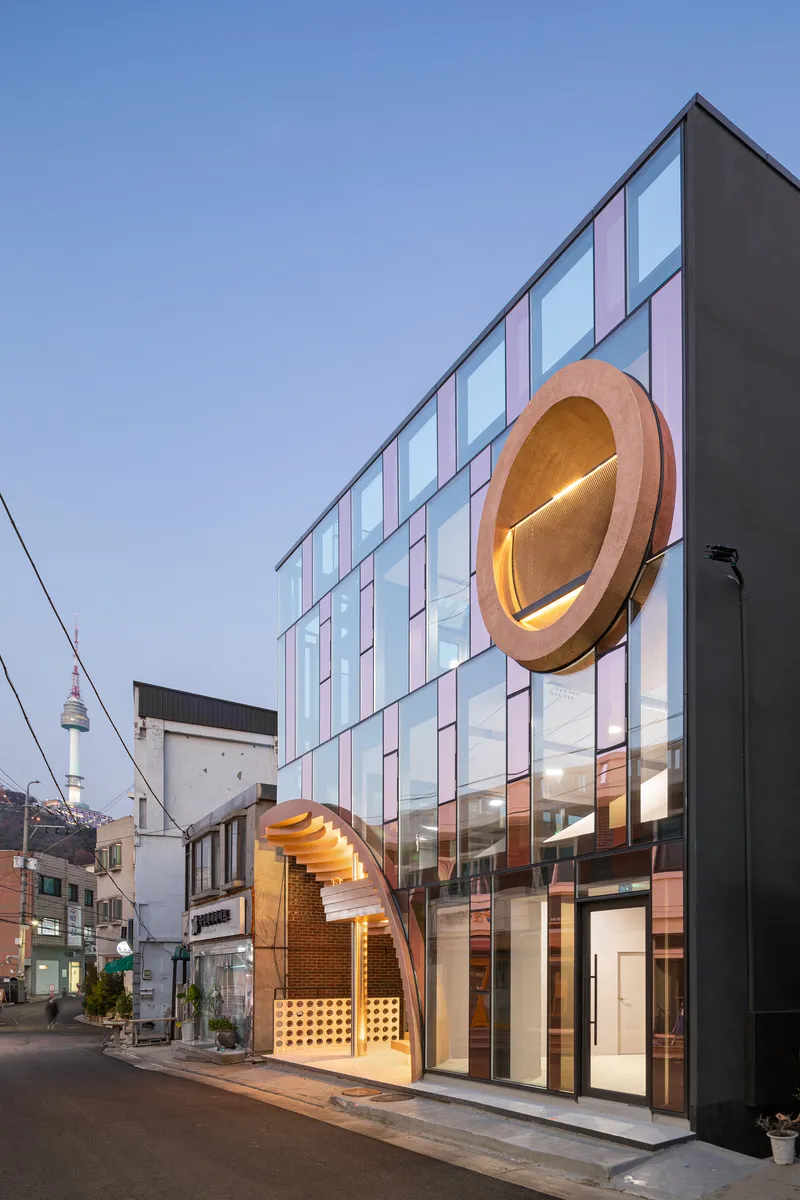 Evening view of the glass facade and circular timber porthole element illuminated from within at dusk