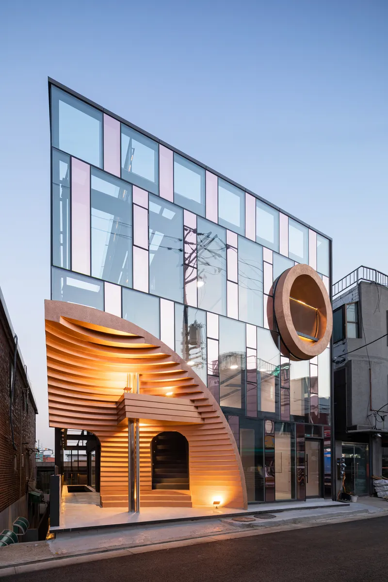 Layered timber arch canopy with integrated lighting beside the gridded glass facade at twilight