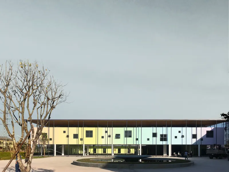 Front elevation showing the pastel-paneled facade with cantilevered overhang and bare tree beside a circular fountain
