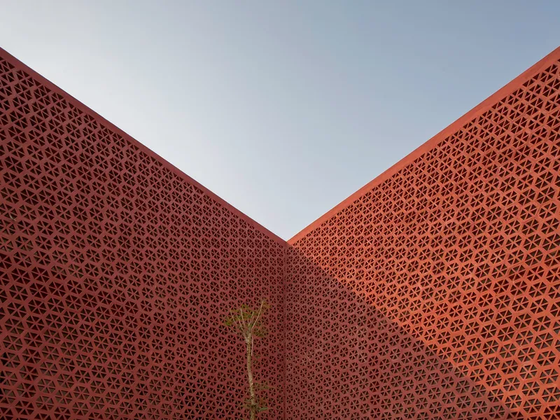 Courtyard view looking up at converging perforated terracotta screen walls with a small tree at the corner