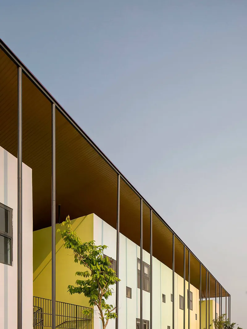 Long sloped roof with wood soffit extending over white facade volumes and a planted courtyard at dusk