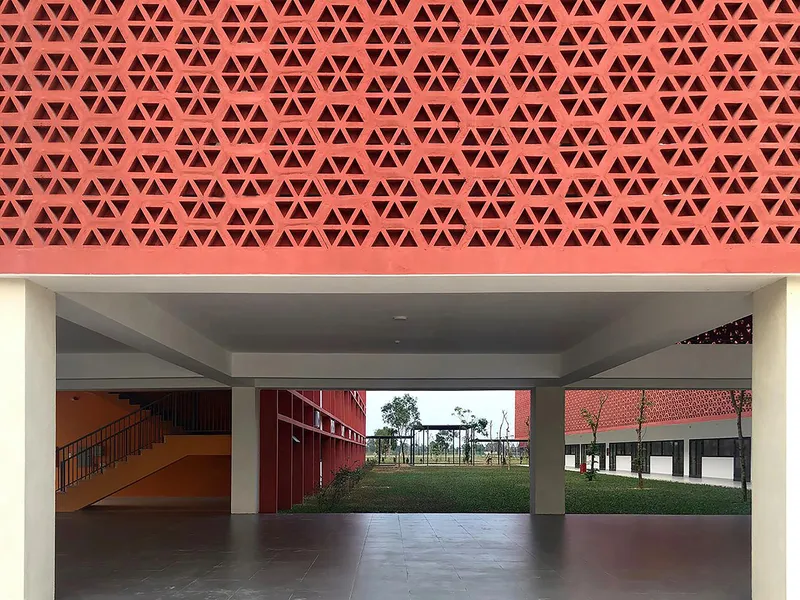 Covered corridor with terracotta geometric screen overhead and view through concrete columns to planted lawn