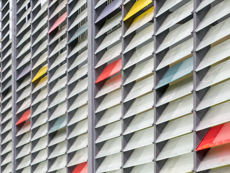 Close-up of angled metal louver facade with white fins accented by scattered yellow and orange blades