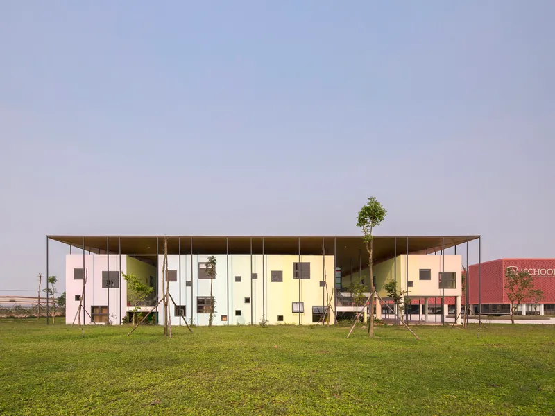 Long facade with thin roof overhang sheltering glass and panel volumes across a lawn