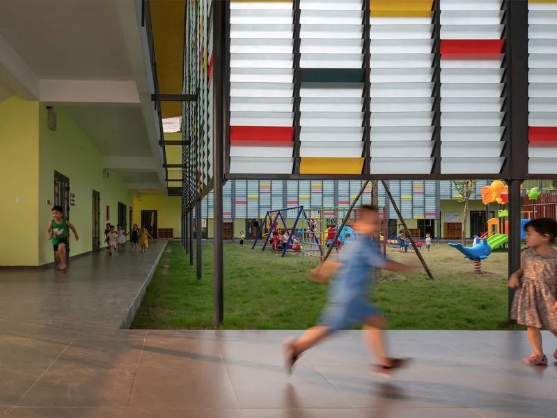 Covered courtyard with playground equipment and children in motion between classroom corridors