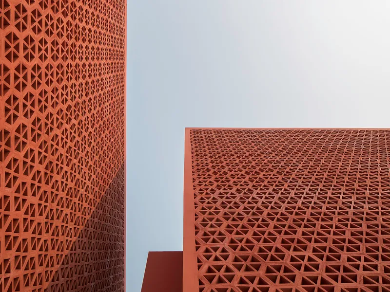 Upward view of geometric terracotta lattice panels wrapping two walls at a corner