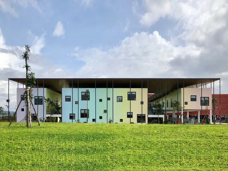 Long view of the pastel-colored facade with scattered square windows above a lawn under scattered clouds