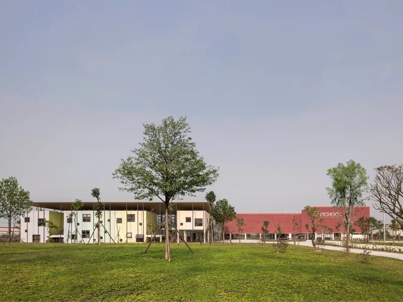 Campus view with the two-story facade and brick volume beyond a grassy field and young trees