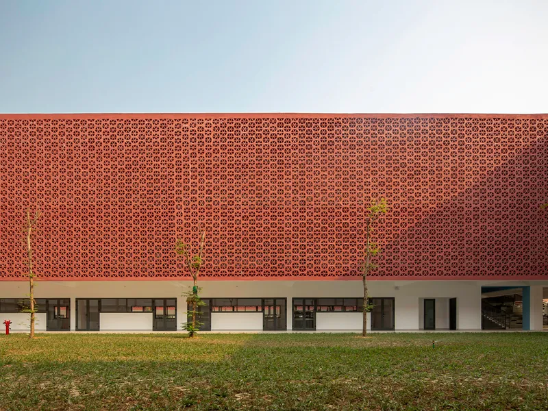 Two-story facade with perforated terracotta screen above white columns and planted saplings on grass lawn