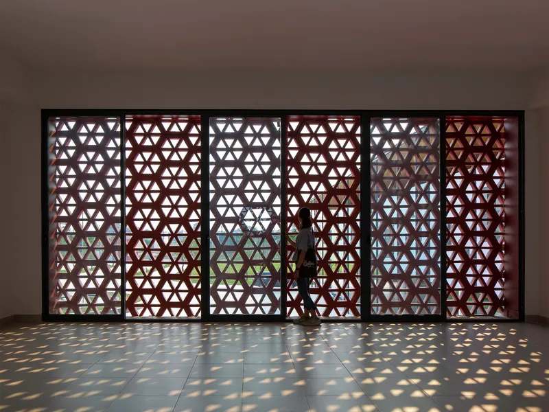 Interior corridor with triangular patterned screen wall casting dappled sunlight on polished floor