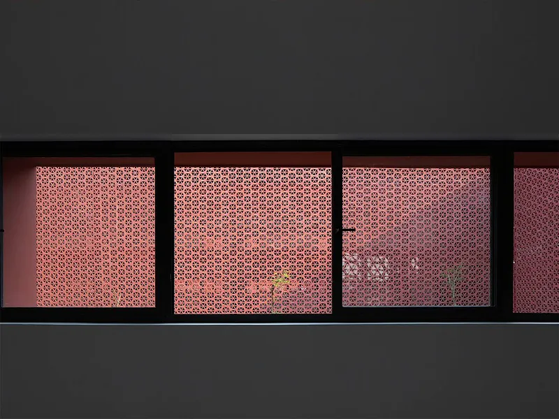 Horizontal strip windows with backlit geometric perforated screens in coral pink tones at dusk