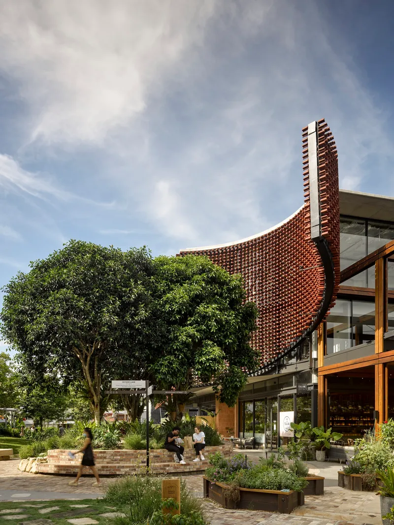 Curved perforated brick screen rising above glazed ground floor and landscaped courtyard with mature trees