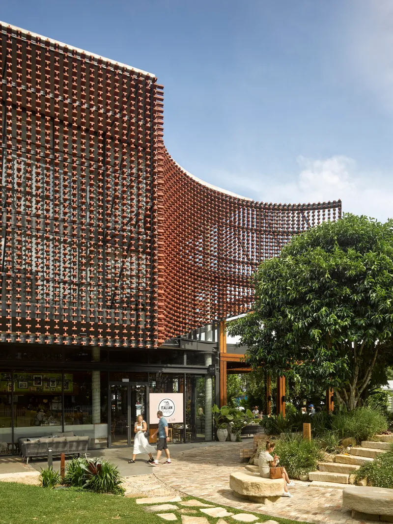 Undulating perforated brick facade with pedestrians walking beneath the cantilevered screen on paved path