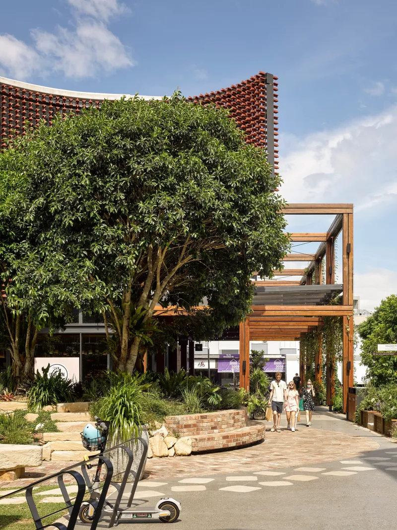 Timber pergola structure and mature tree framing the perforated brick screen facade under cloudy skies