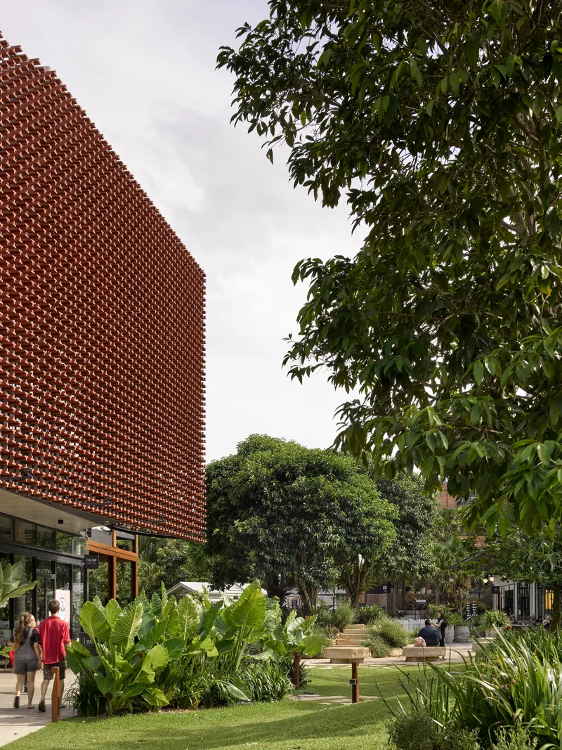 Perforated brick wall rising above landscaped gardens with tropical plantings and visitors on pathways